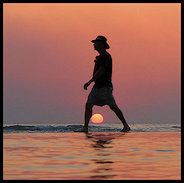 Man walking the beach over the sun